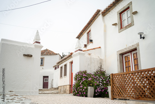 Fototapeta Naklejka Na Ścianę i Meble -  Typical streets in Portugal surrounded by white two-storey houses. Small Portugal city Azenhas do Mar with flower fence and beautiful houses. Shot passing by white big house on narrow street