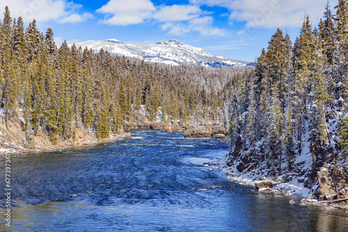 Snow-covered winter landscape of the Yellowstone River, mountain and evergreen forest in Yellowstone National Park Wyoming.