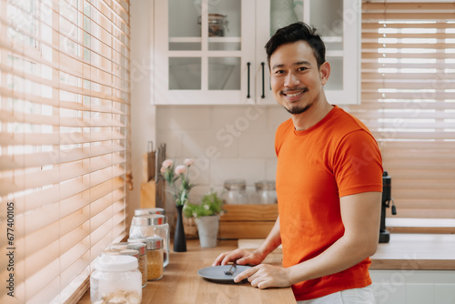 Asian man preparing his easy breakfast in the kitchen in warm light morning. © Sevendeman