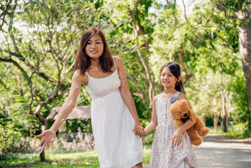Happiness mother daughter play together in green garden park outdoor lifestyle. Happy family two people enjoy have fun cheerful smile best friends. Asian cute childhood play bubble with teddy bear © aFotostock