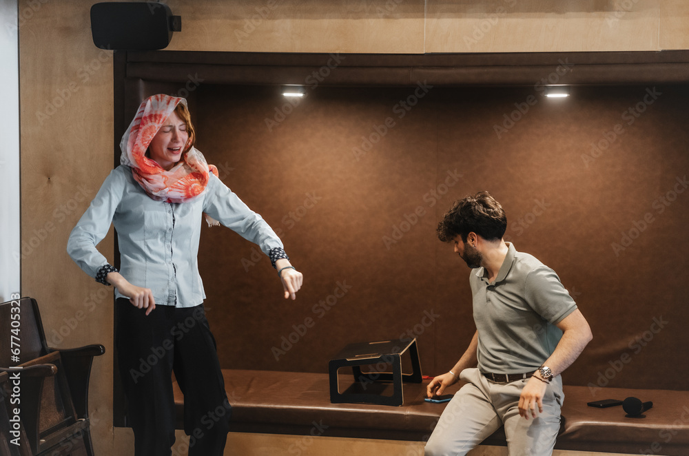 Muslim woman having fun during office break hours with her coworker who is sitting in a recessed sofa area
