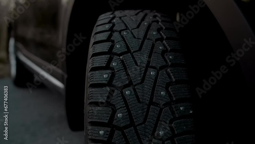 Close-up and tilting of a new tyre with winter spikes on the front wheel of a black car photo