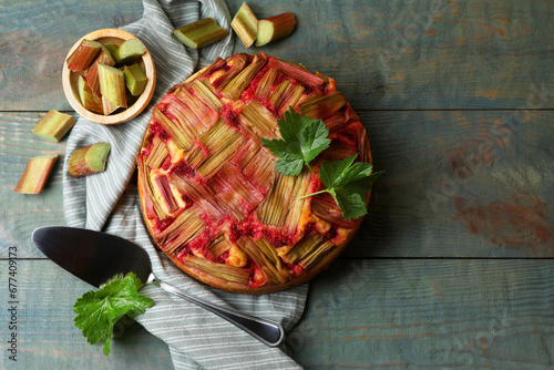 Freshly baked rhubarb pie, cut stalks and cake server on wooden table, flat lay. Space for text