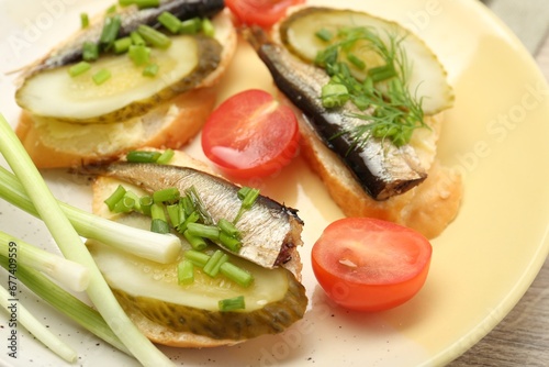 Delicious sandwiches with sprats, pickled cucumber and green onion served with tomato on wooden table, closeup