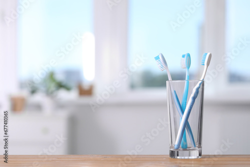 Plastic toothbrushes in holder on wooden table indoors. Space for text