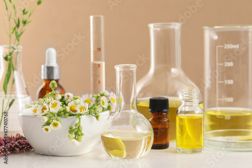 Developing cosmetic oil. Laboratory glassware and flowers on white wooden table