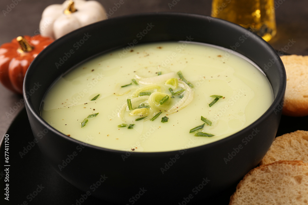 Bowl of tasty leek soup and bread on table, closeup