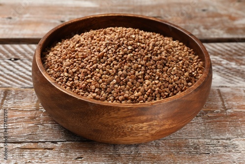 Bowl with dry buckwheat on wooden table, closeup