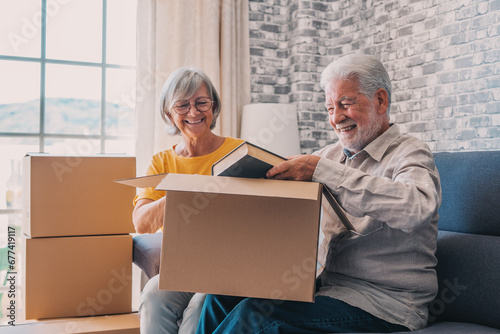 Relaxed mature married couple in love resting on couch among paper cardboard boxes, taking break, pause, hugging, talking, enjoying being in new home. Real estate concept.