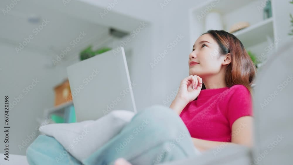 Happy young Asian woman using laptop while seated on couch at home Happy young Asian woman using laptop while seated on couch at home