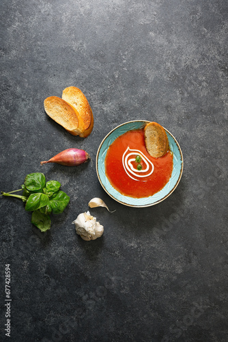 Cream of tomato and basil soup in bowl on black background with ingredients around