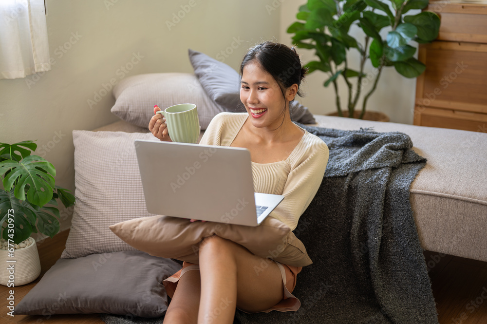 A cheerful woman is enjoying talking on a video call with her friend on her laptop in her bedroom. A cheerful woman is enjoying talking on a video call with her friend on her laptop in her bedroom.