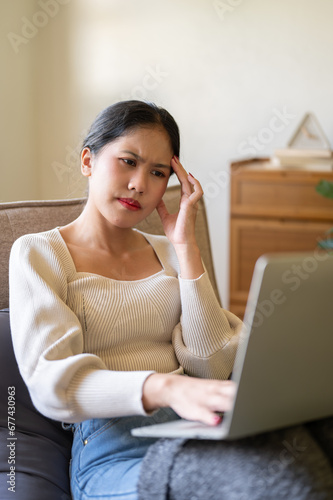 A confused Asian woman is reading an online article on the website while sitting on a couch.