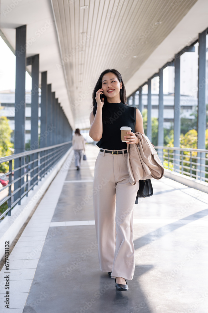 A confident and busy Asian businesswoman is talking on the phone while going to her office.