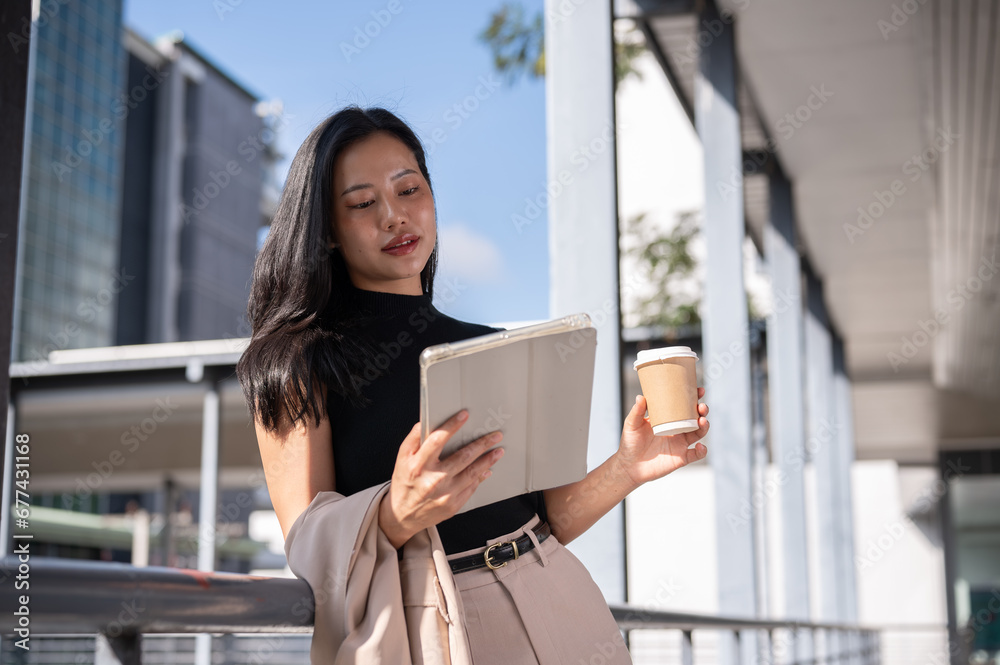 An attractive businesswoman is checking a project online on her tablet while she is on a skywalk.
