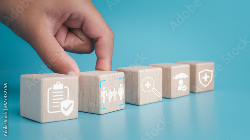 Health insurance and healthcare concept, human hand holds wooden block with icons about health insurance and healthcare access, retirement planning on blue background.