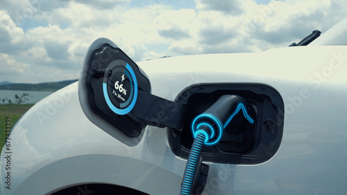 Electric car plug in with charging station, recharge battery by EV charger cable display smart digital battery status hologram with nature background. Futuristic green energy infrastructure.Peruse