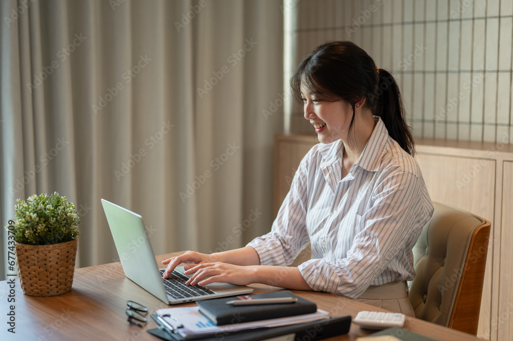 A beautiful Asian businesswoman working on her laptop at a meeting table in a meeting room alone.