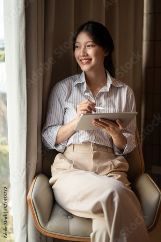 Beautiful woman is looking out the window, thinking about some creative ideas while using her tablet
