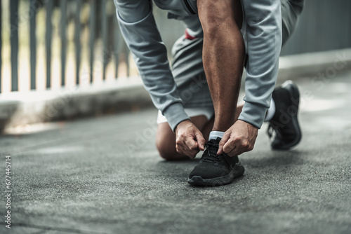 A man tying shoelaces on sport shoes in the city center park before cardio workout, running. Health and Lifestyle in big city life concept.