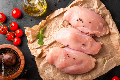 Raw chicken breast meat and spices for its preparation on a black background, top view photo