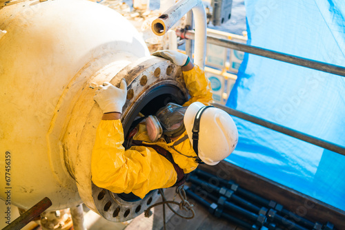 A high-pressure tank inspector enters a confined space in a petroleum chemical protective suit. photo