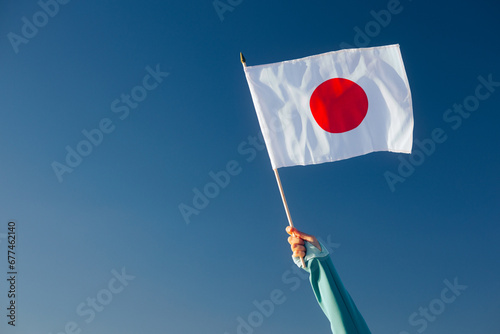 Hand Waiving a Japanese Flag on a Blue Sky. Cheerful enthusiastic patriotic person displaying the symbol of Japan
 photo