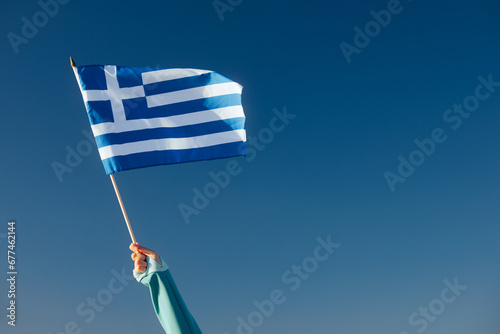 Fotografie Hand Waiving a Greek Flag on a Blue Sky