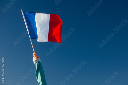 Hand Waiving an French Flag on a Blue Sky. Cheerful enthusiastic patriotic person displaying the symbol of France
 photo