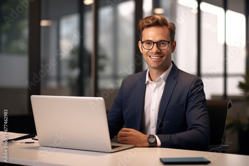 businessman works on a laptop computer. He looks at the camera with a smile.