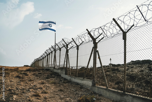 Tableau sur toile View of israeli flag behind barbed wire against cloudy sky in the desert