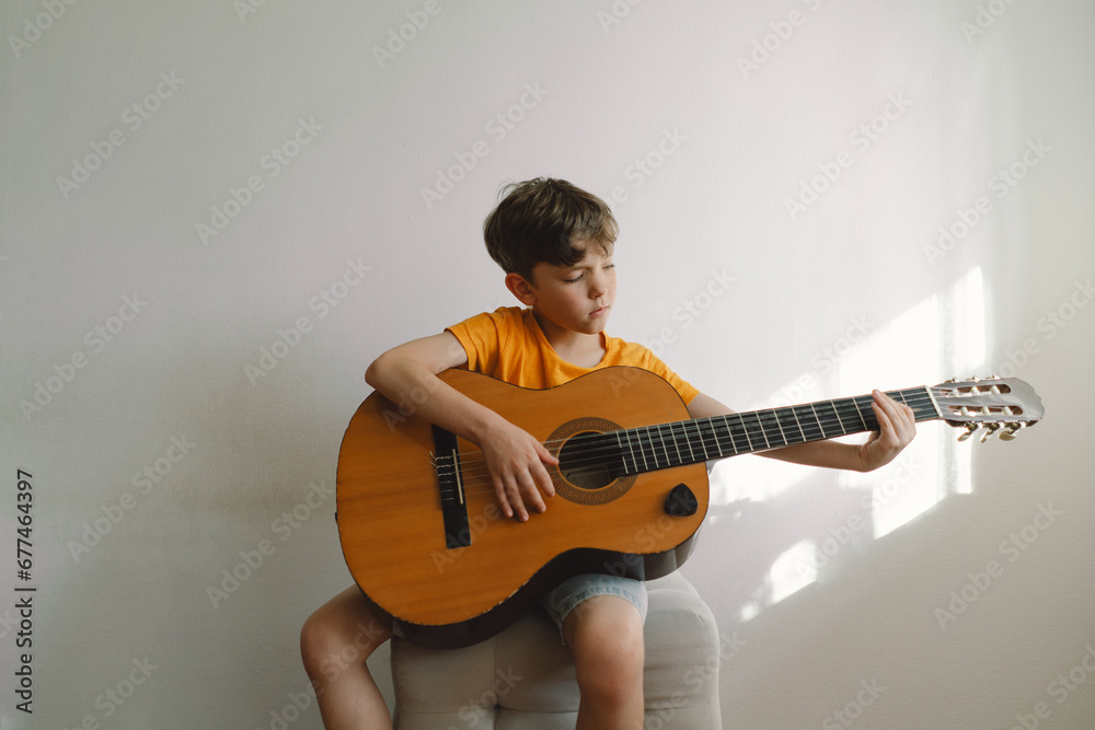 Cute boy learns to play the classical guitar in home. Cozy home. Summer holidays lifestyle. Cute boy learns to play the classical guitar in home. Cozy home. Summer holidays lifestyle.