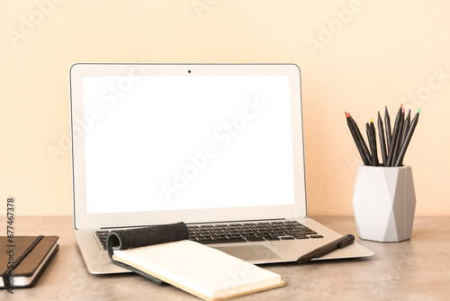 Modern laptop, notebooks and holder with different pencils on desk