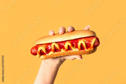Принти на полотні Woman holding tasty hot dog on yellow background