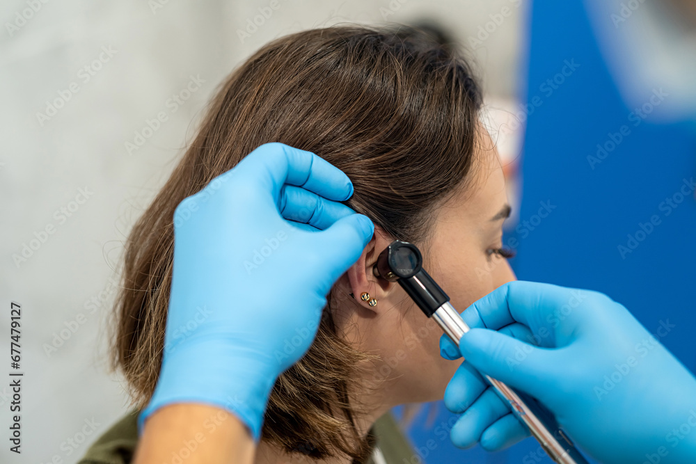 Advanced examination of a woman's ear using an otoscope at a doctor's appointment. - obrazy, fototapety, plakaty 
