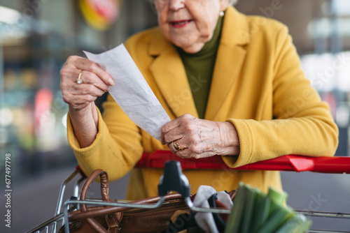 Elderly woman checking her receipt after purchase, looking at amount of money spent, ensuring all charges are correct. photo