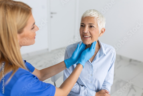 medicine, healthcare and medical exam concept - doctor or nurse checking patient's tonsils at hospital. Endocrinologist examining throat of senior woman in clinic photo