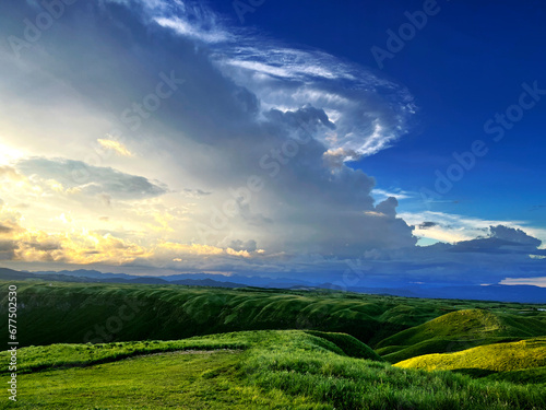 the nature mountain ridge landscape sunrise or sunset view is a green grass meadow and highland hill glen mountain with white cloud cloudy cloudscape on a blue beautiful bright sunlight sky background