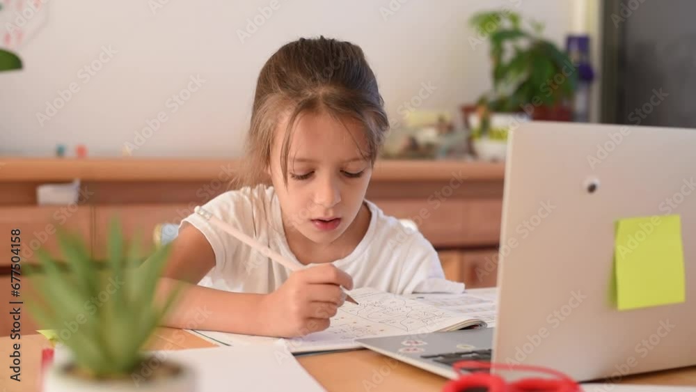 Child study at home. Girl in white t-shirt sit in table write note on copybook and study with zoom online infront of laptop. Kid hold the hand on head with thoughtful face task exercise Child study at home. Girl in white t-shirt sit in table write note on copybook and study with zoom online infront of laptop. Kid hold the hand on head with thoughtful face task exercise