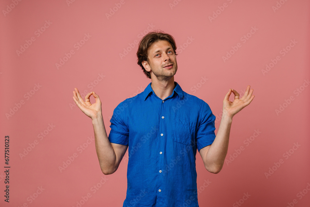 Young man meditating with zen fingers isolated over pink wall Young man meditating with zen fingers isolated over pink wall