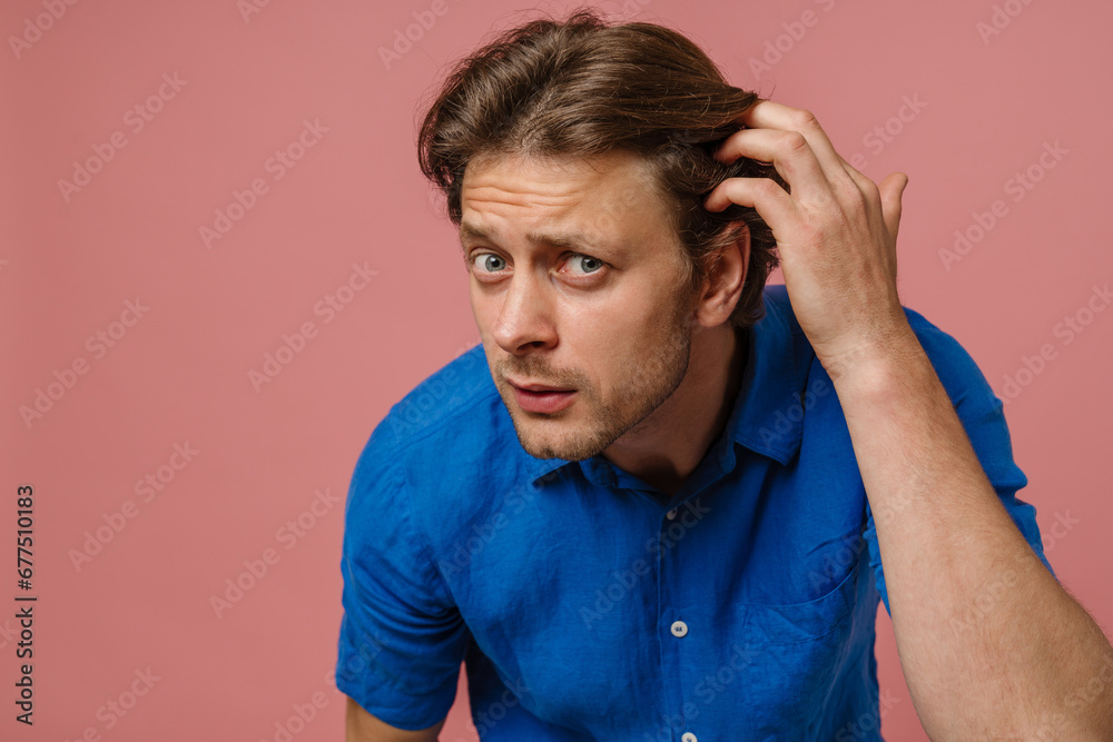 Young man touching his hair and looking at camera as at mirror isolated over pink wall Young man touching his hair and looking at camera as at mirror isolated over pink wall