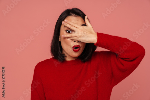 Young woman covering her eye with hand while standing over isolated pink background © Drobot Dean