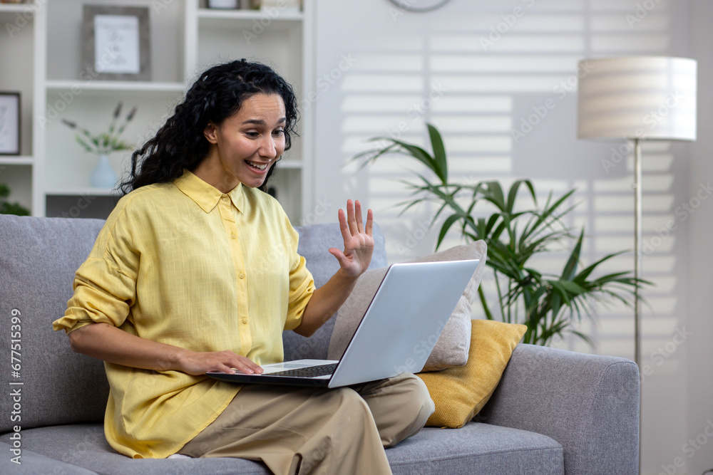 Happy hispanic woman sitting on sofa in bright living room with laptop on lap, video calling, distance learning, work meeting from home. Happy hispanic woman sitting on sofa in bright living room with laptop on lap, video calling, distance learning, work meeting from home.