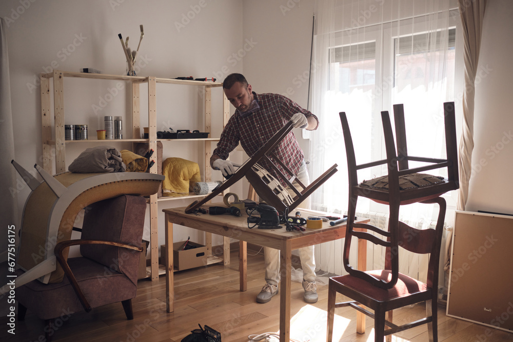 Man working in a small home workshop for furniture repairing and restoration. Man working in a small home workshop for furniture repairing and restoration.