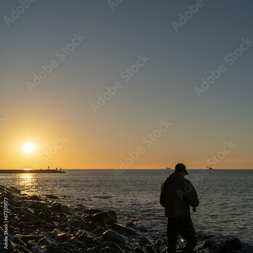 silhouette of a fly fisherman catching sea trout at dawn in the sea
