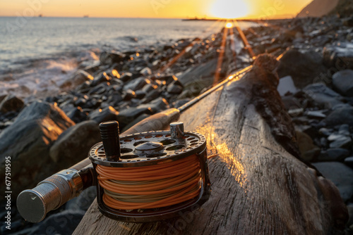 A fly fishing rod and an open fly fishing box lie on the sea rocks at sunset © Michael