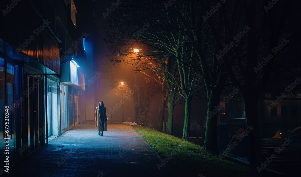 A lone walker on illuminated city streets at midnight. A lone walker on illuminated city streets at midnight.