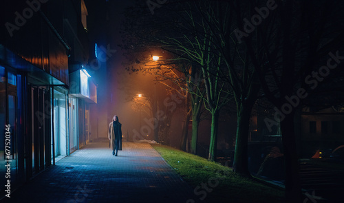 A lone walker on illuminated city streets at midnight.