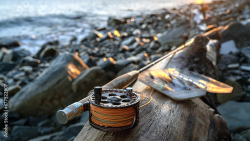 A fly fishing rod and an open fly fishing box lie on the sea rocks at sunset. photo