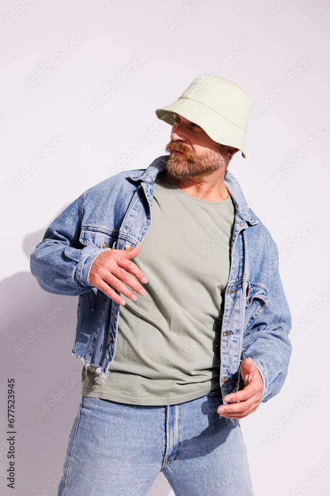 Stylish bearded man in denim jacket and green bucket hat posing on grey Stylish bearded man in denim jacket and green bucket hat posing on grey